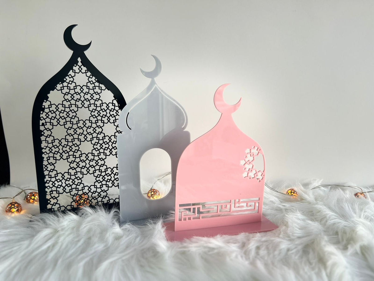 ثلاث قطع رمضانية من الأكريليك على شكل مسجد، بالأسود المزخرف والأبيض والوردي، بخط كوفي، تضيئها أنوار صغيرة