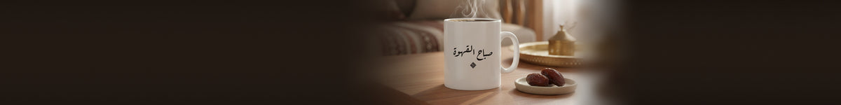 A white ceramic mug printed «صباح القهوة», steaming, beside a plate of dates on a coffee table