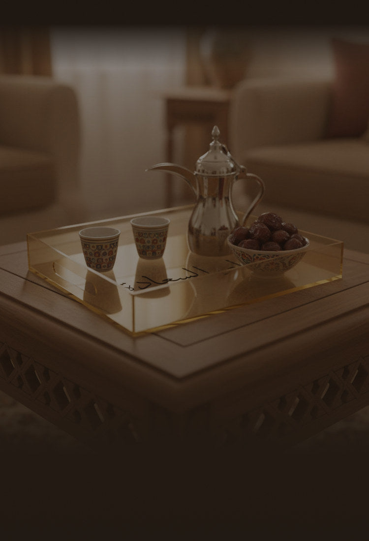A gold-tinted acrylic serving tray engraved «دار السعادة», with a dallah, coffee cups and dates, on a carved wooden table