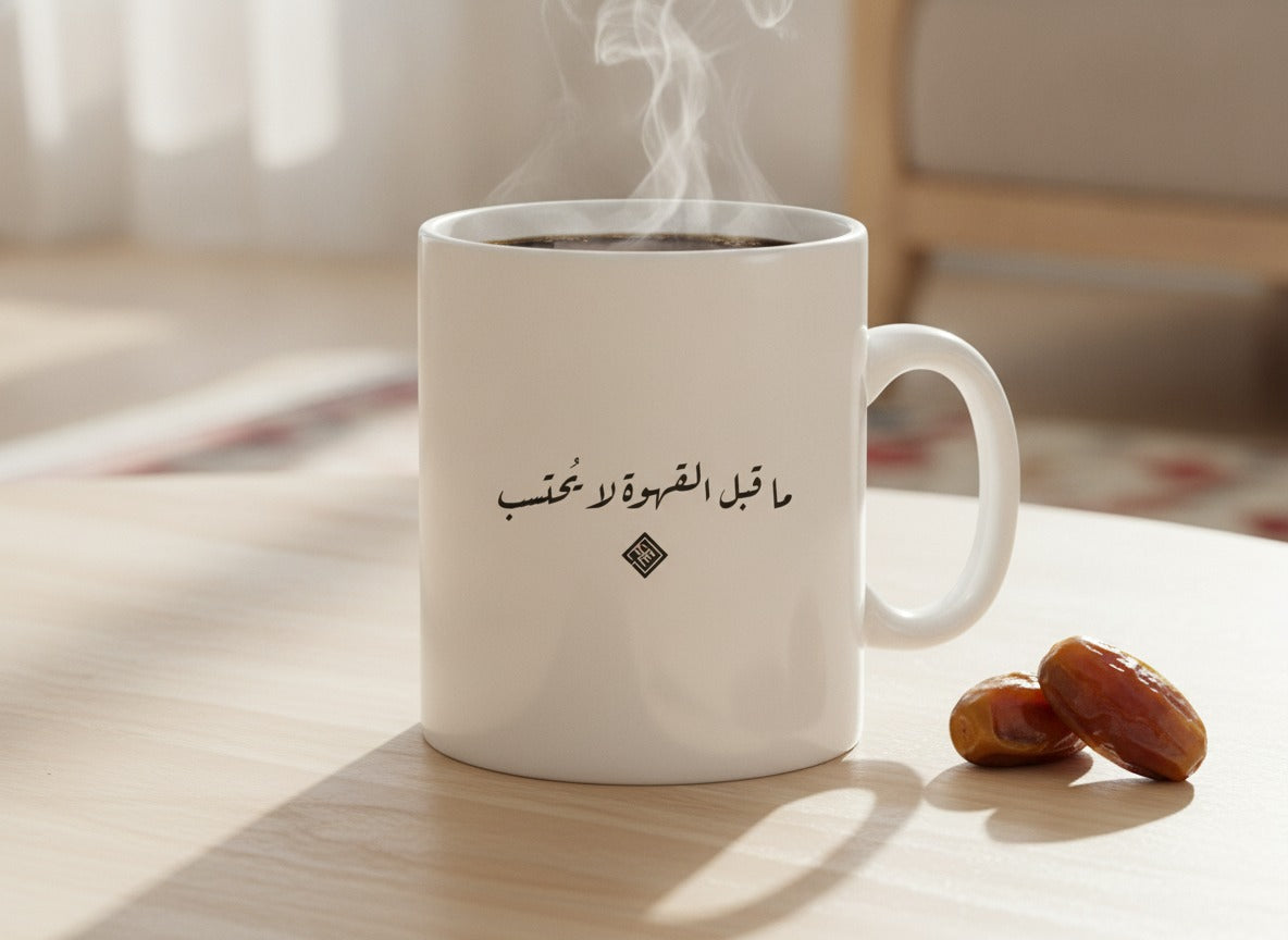 «ما قبل القهوة لا يُحتسب» calligraphy mug, filled, on a coffee table
