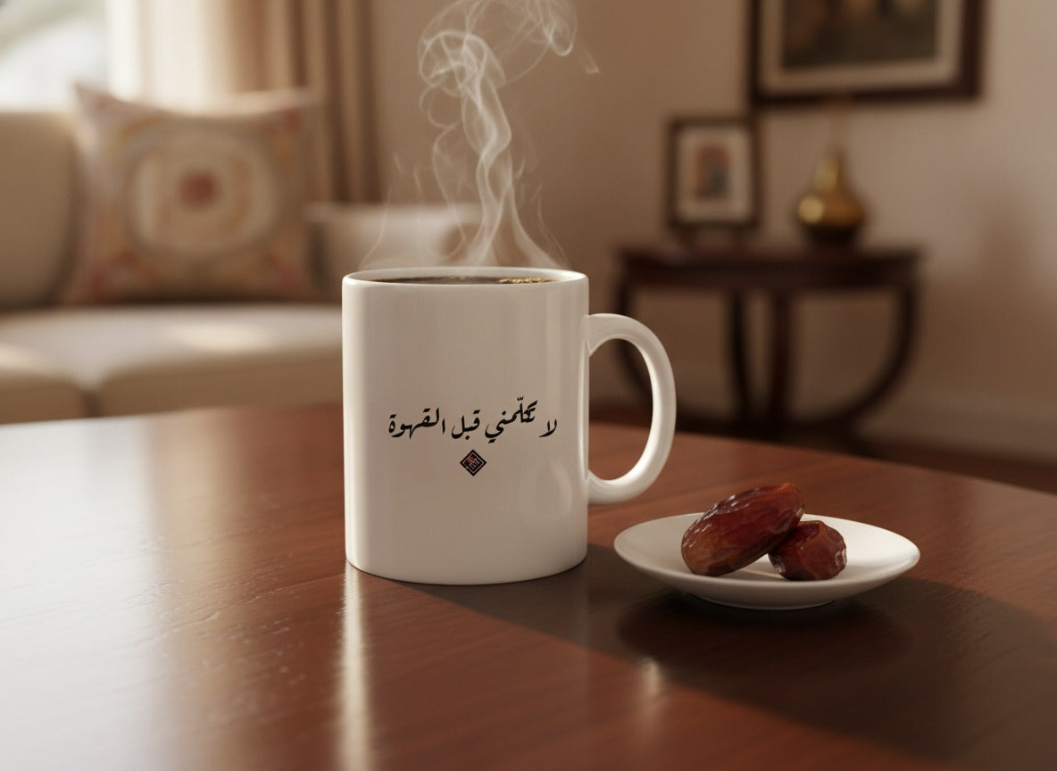 «لا تكلّمني قبل القهوة» calligraphy mug, filled, on a coffee table