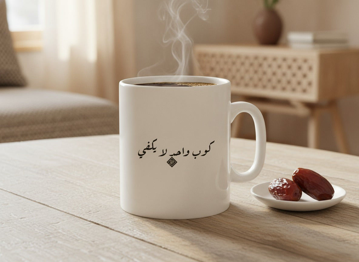 «كوب واحد لا يكفي» calligraphy mug, filled, on a coffee table